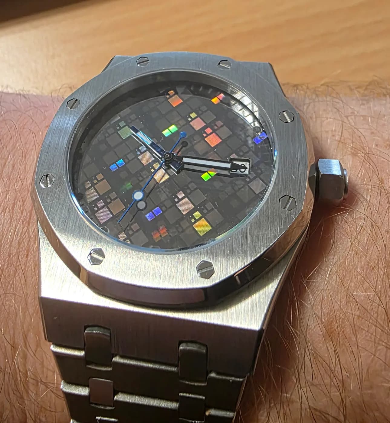 Montre Silicium au poignet : boîtier octogonal en acier brossé à huit vis, cadran gris sombre quadrillé de carrés irisés bleu, vert, orange et rose.